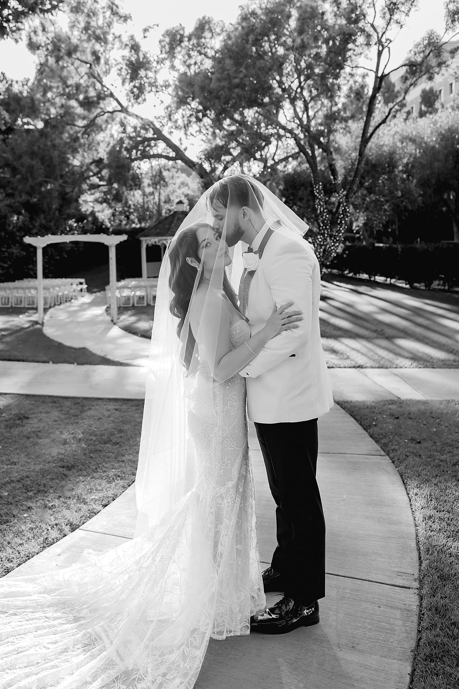 husband and wife stand under veil on sidewalk by Desiree Ashley Photography