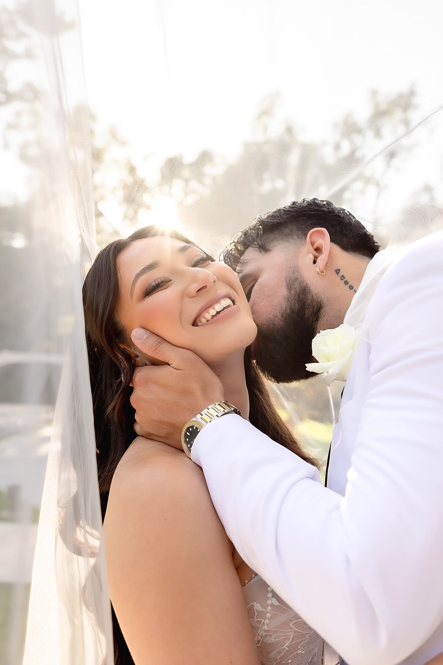 groom leans in to kiss bride's neck under her veil for Summer wedding in Irvine
