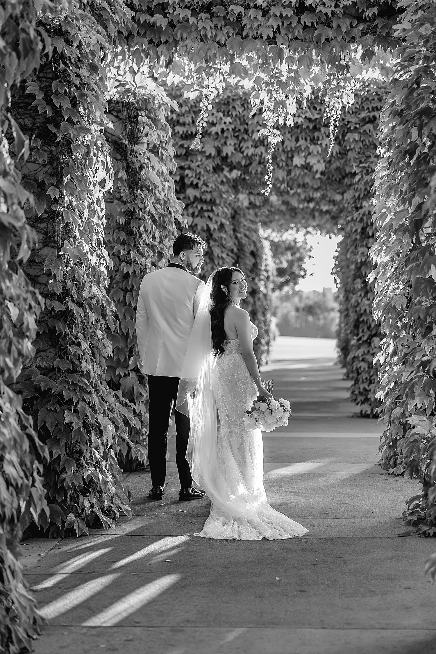 bride looks over her shoulder walking down pathway with husband by Desiree Ashley Photography