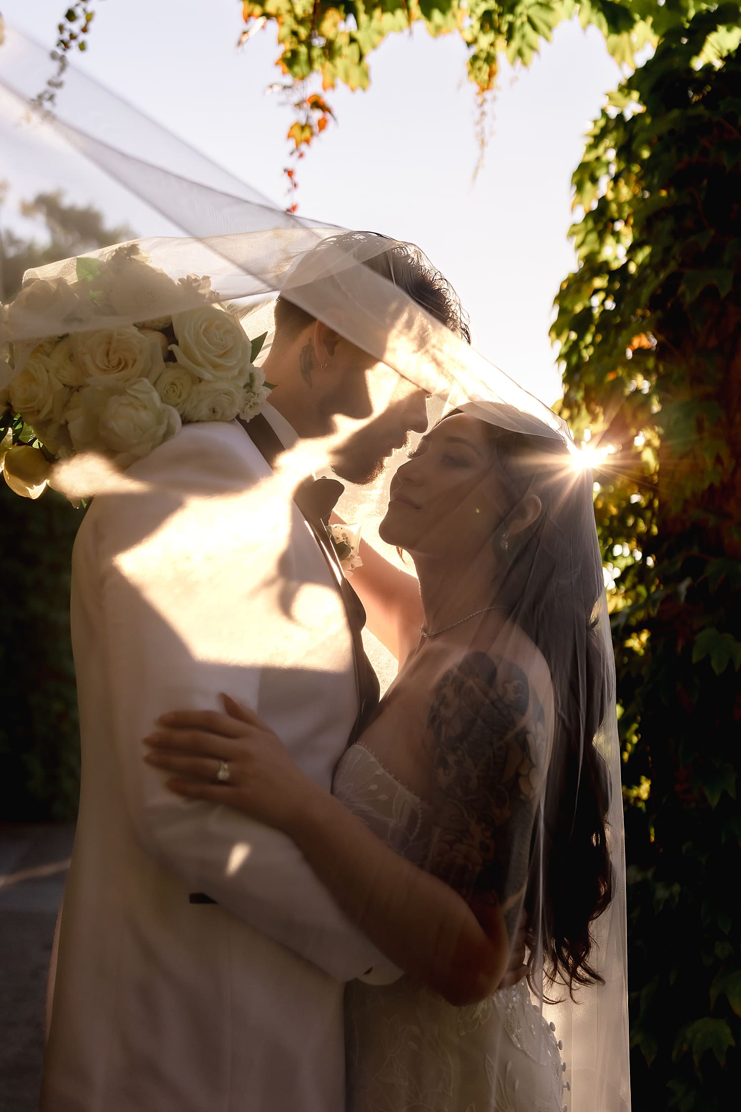 newlyweds stand in setting sun under her veil for Summer wedding in Irvine
