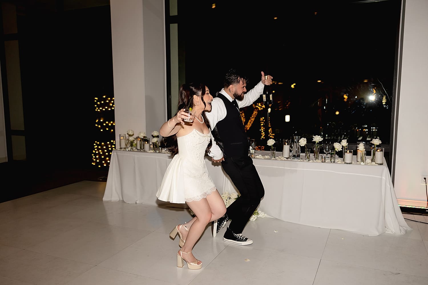 man and woman dance into their reception with drinks in hand for Summer wedding in Irvine