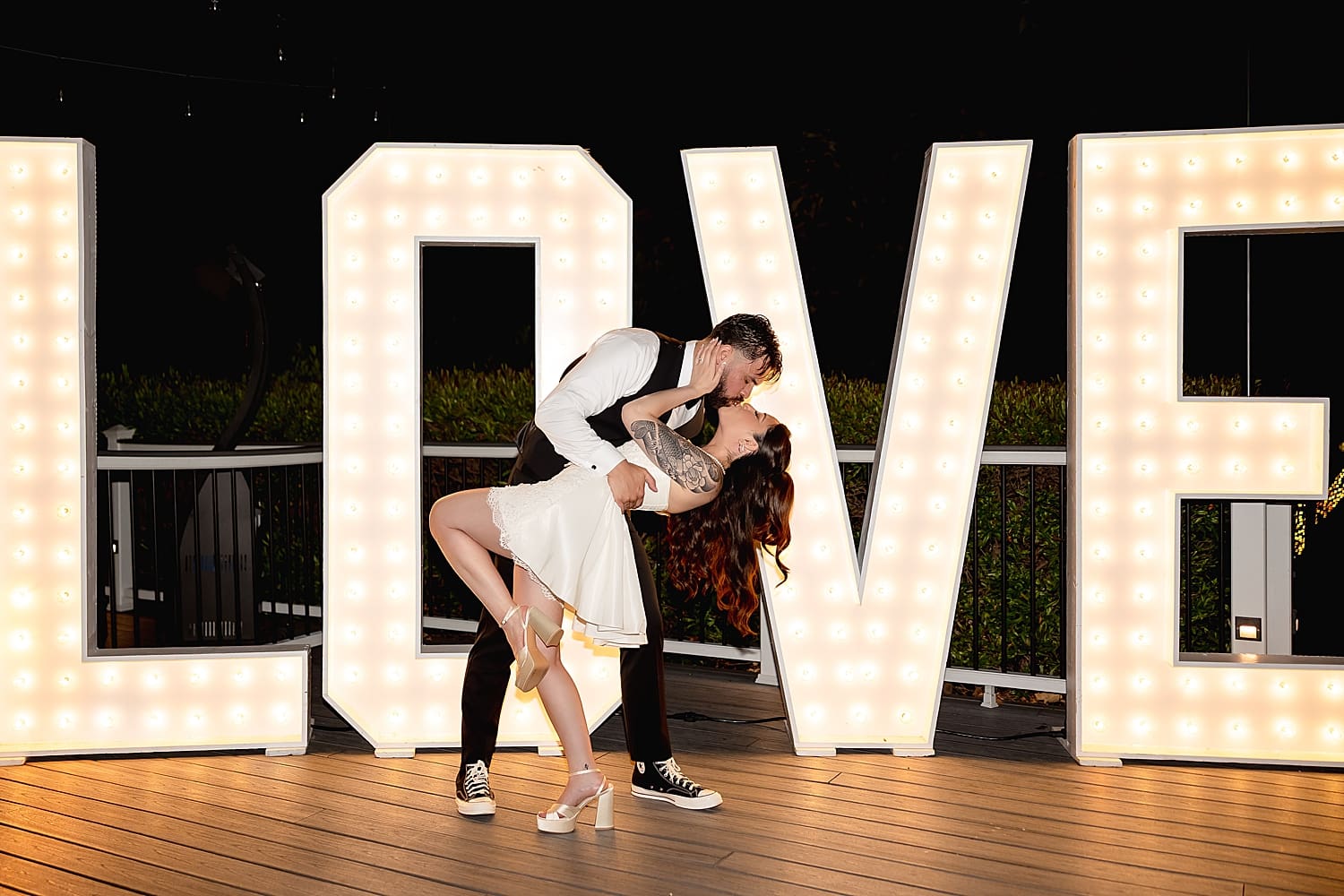 man dips his new wife for a kiss in front of LOVE sign by Desiree Ashley Photography