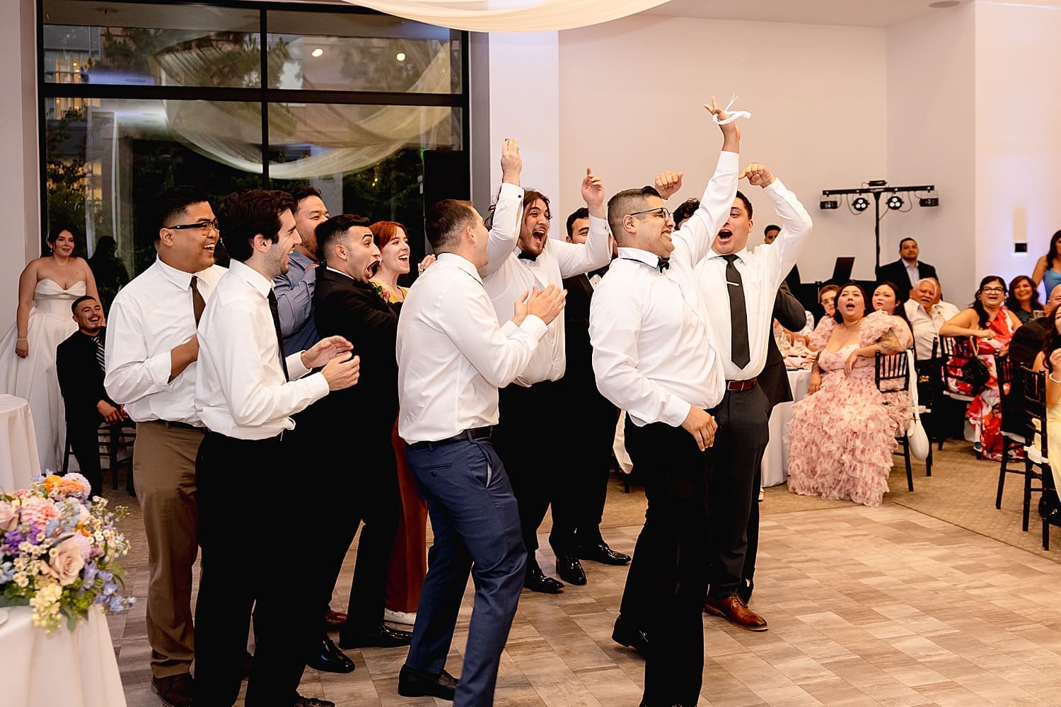 men throw hands in the air with garter at reception by Southern California wedding photographer