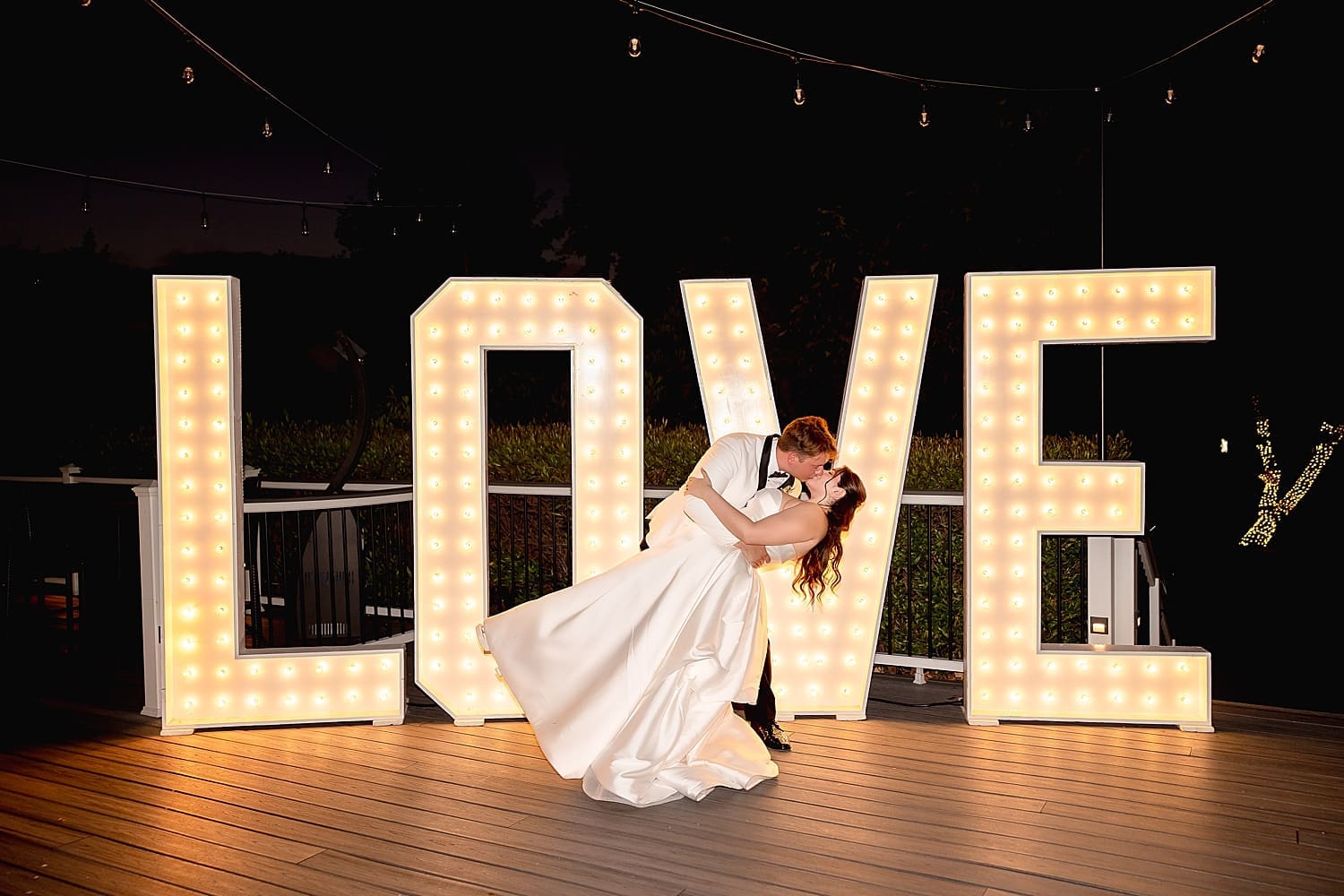 newlyweds dip for a kiss in front of large LOVE letters on patio by Desiree Ashley Photography