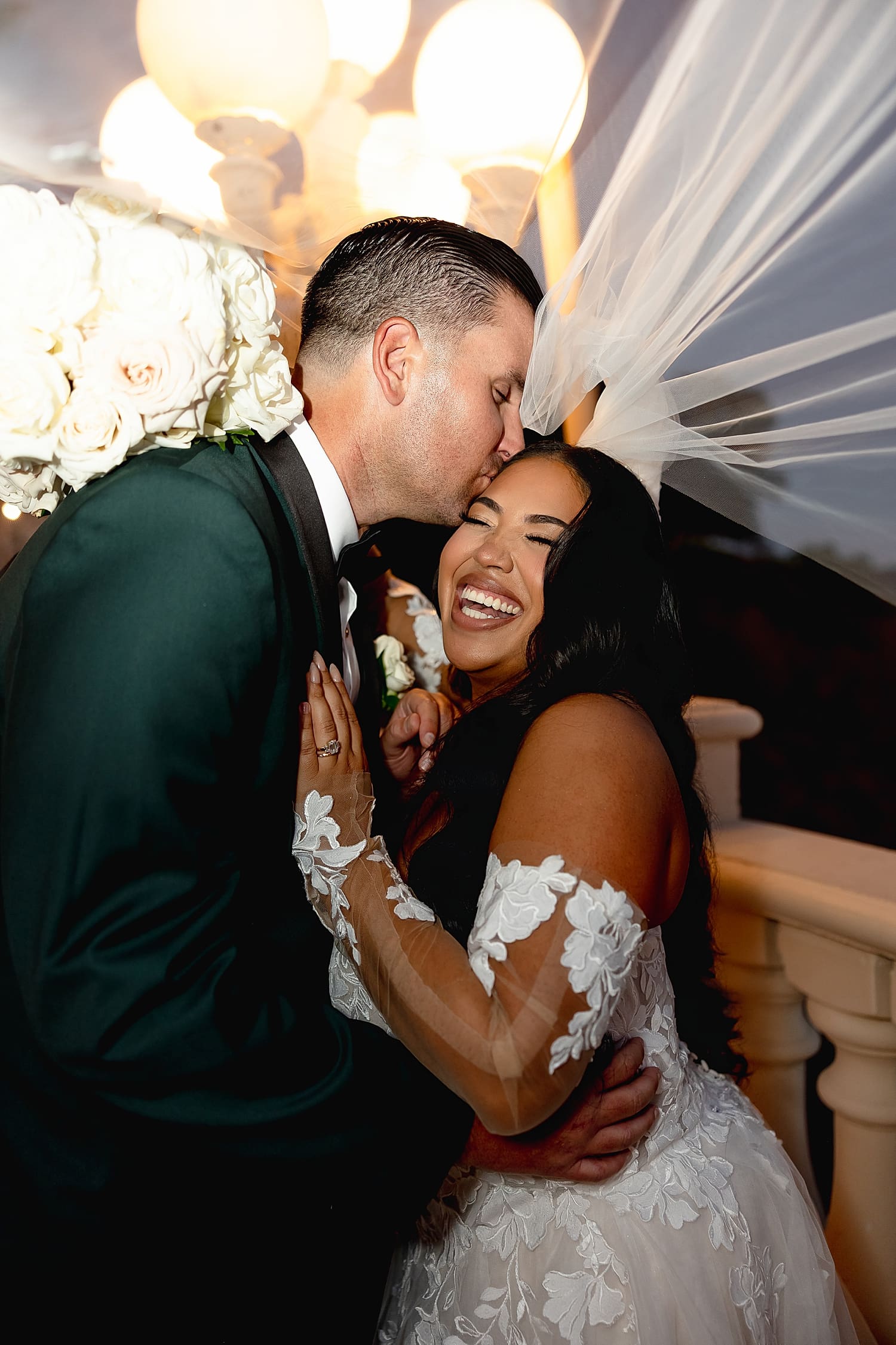 bride giggles as groom kisses her under her veil by Southern California wedding photographer