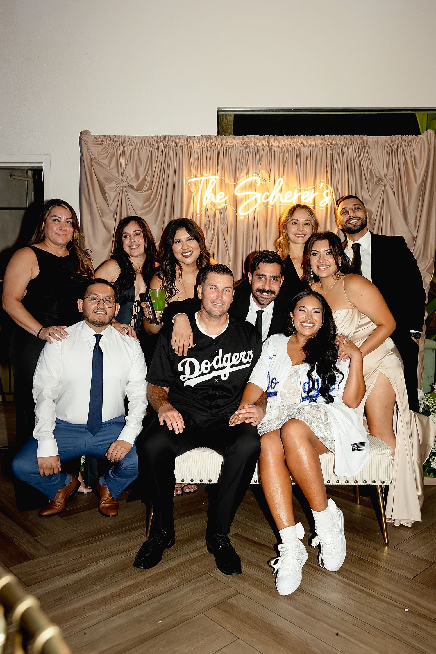 friend group sits together in front of reception backdrop by Desiree Ashley Photography
