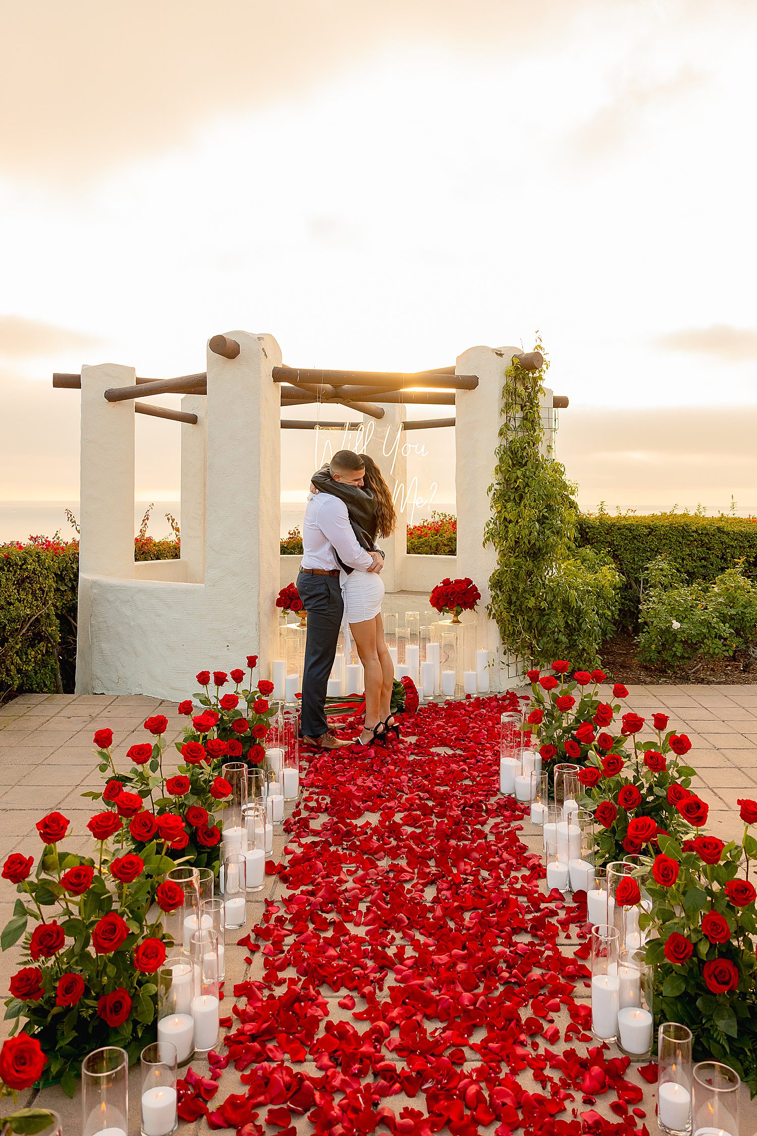 newly engaged couple embrace at end of rose and candle lined path by Desiree Ashley Photography