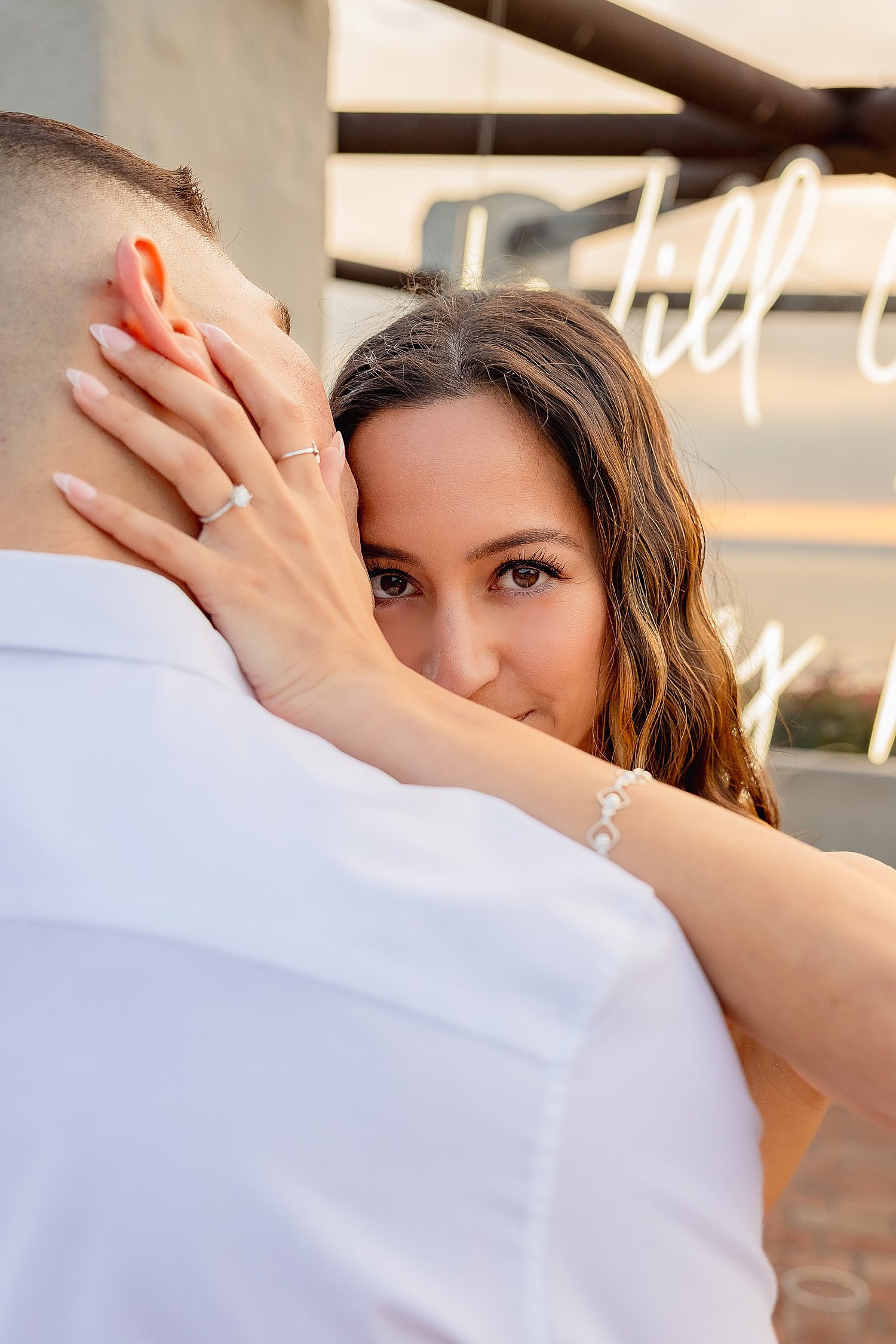 newly engaged bride looks over man's shoulder with her ring on by Southern California wedding photographer
