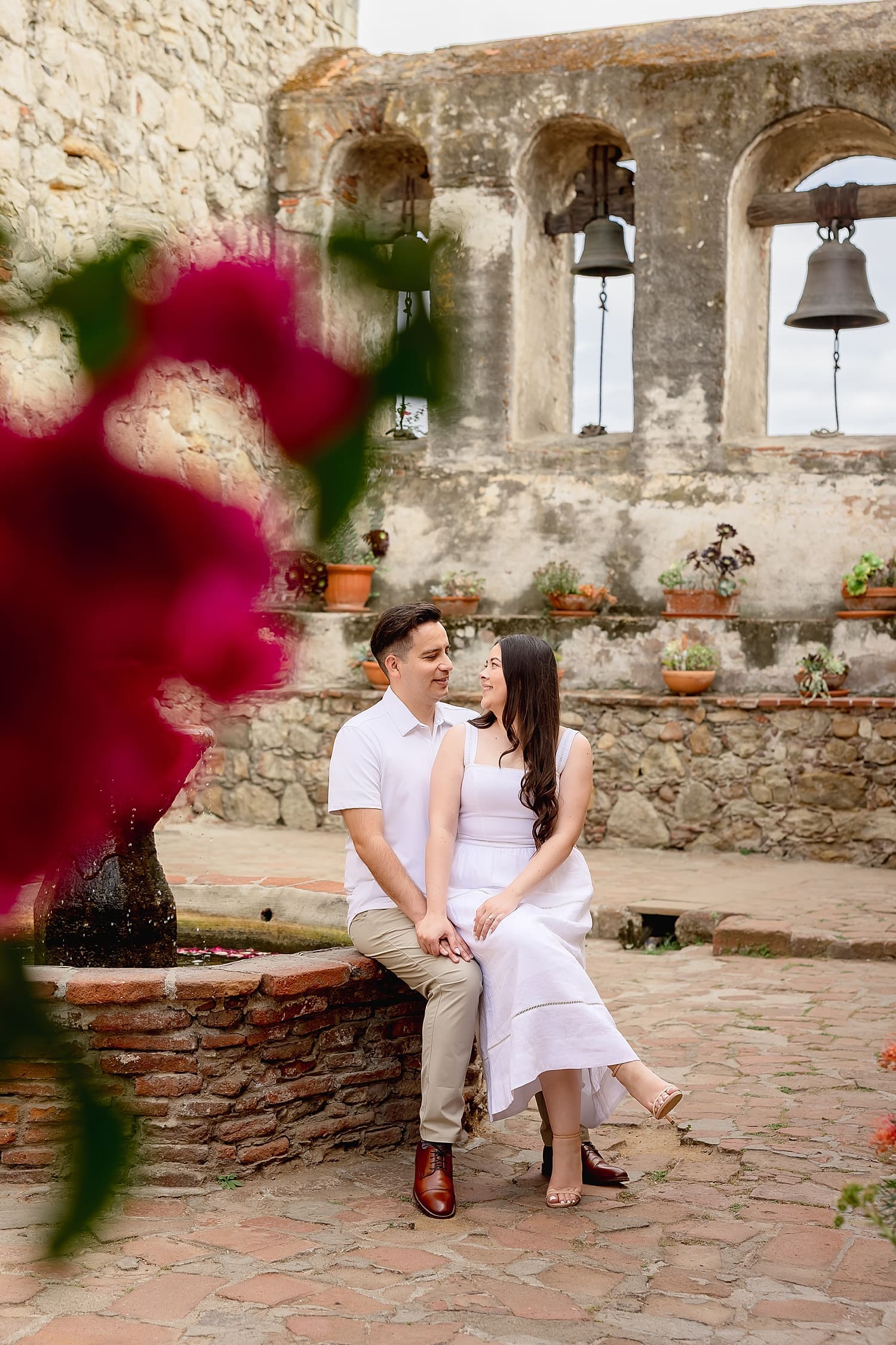 man and woman sit on the edge of old fountain in courtyard by Southern California wedding photographer