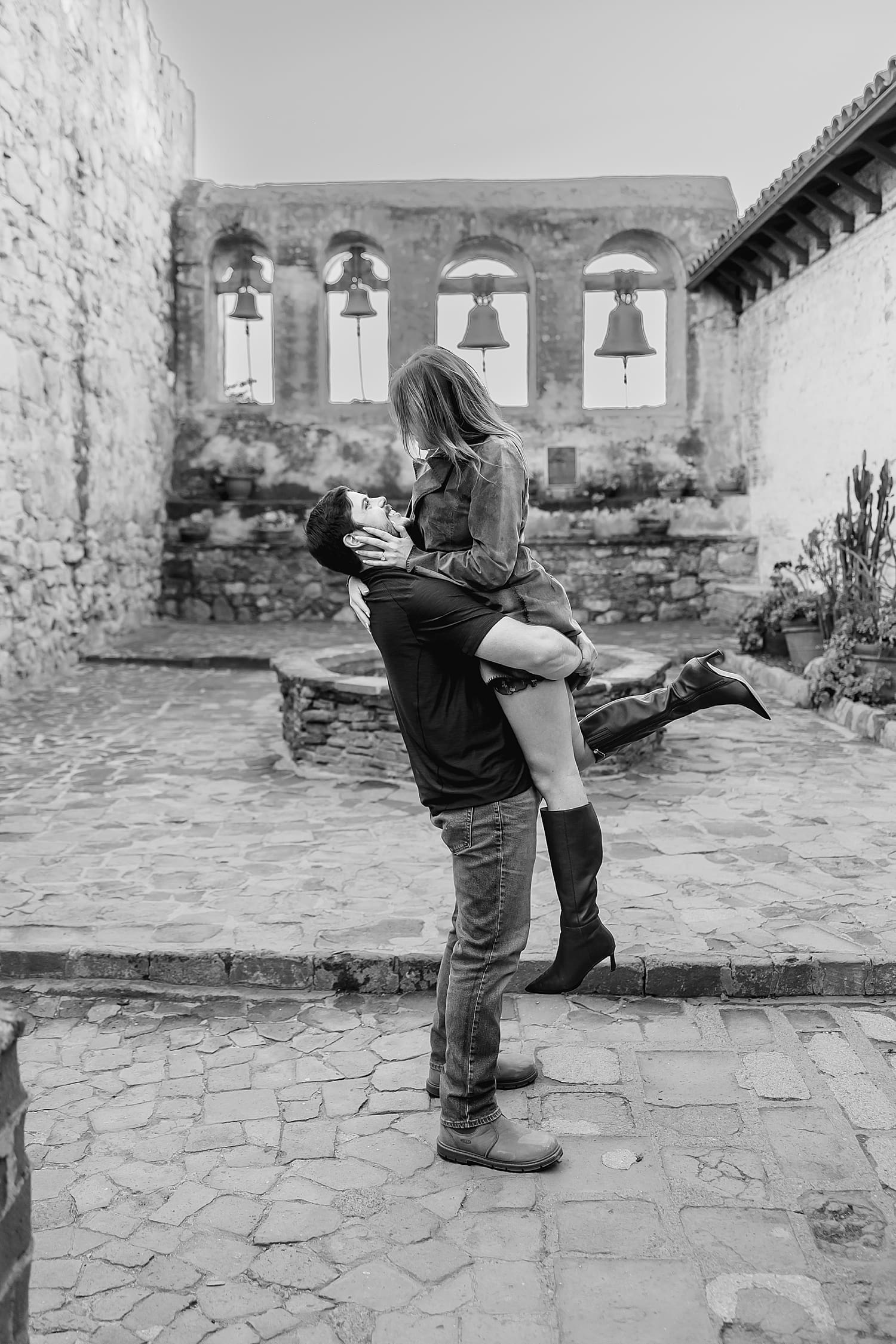Man lifts up his new fiance in embrace at Mission San Juan Capistrano