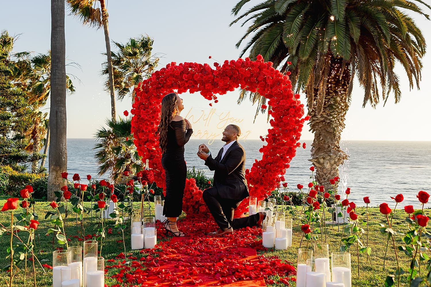 man gets on one knee in front of red rose heart by Southern California wedding photographer