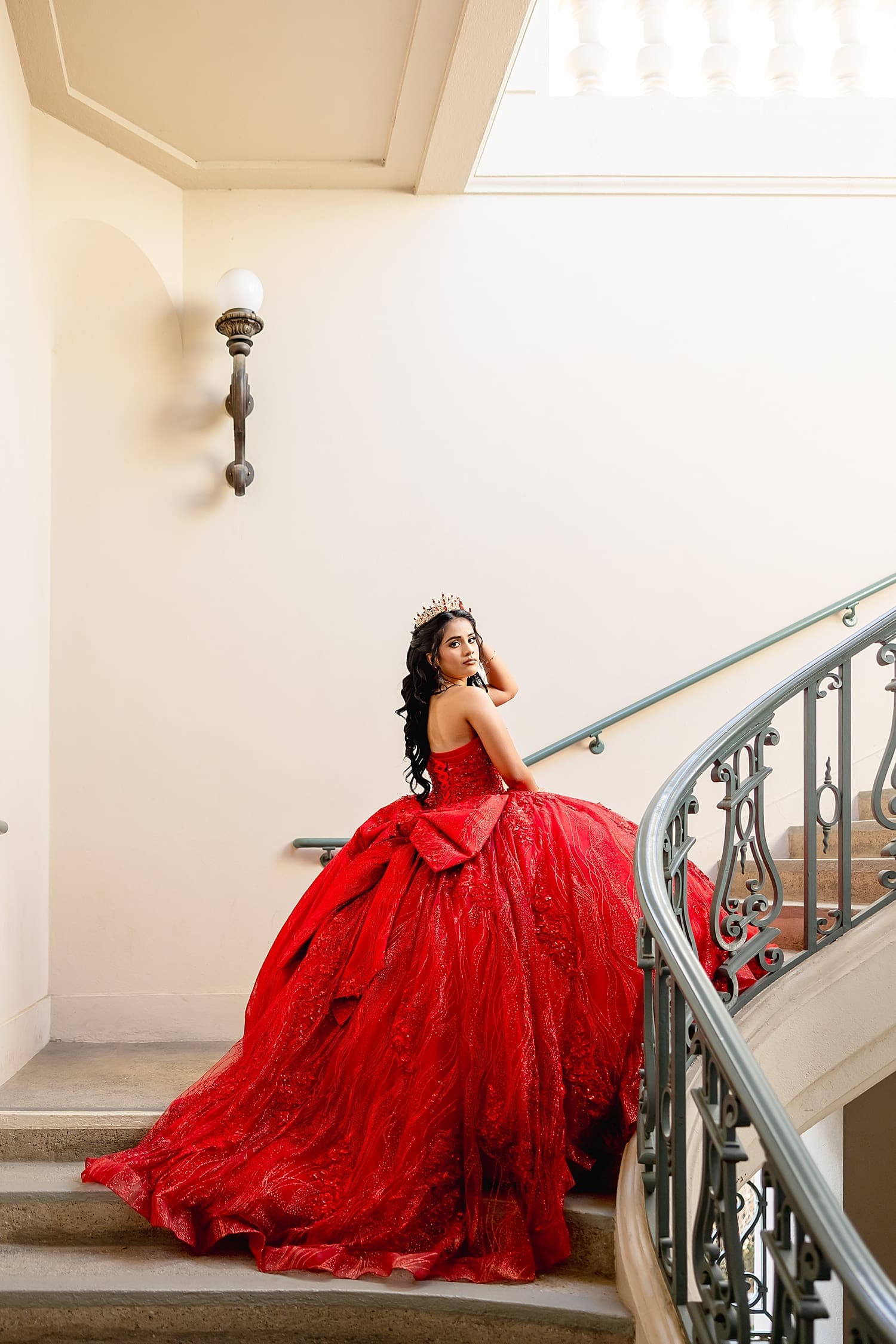 girl in large red dress ascends sweeping staircase by Southern California Wedding Photographer
