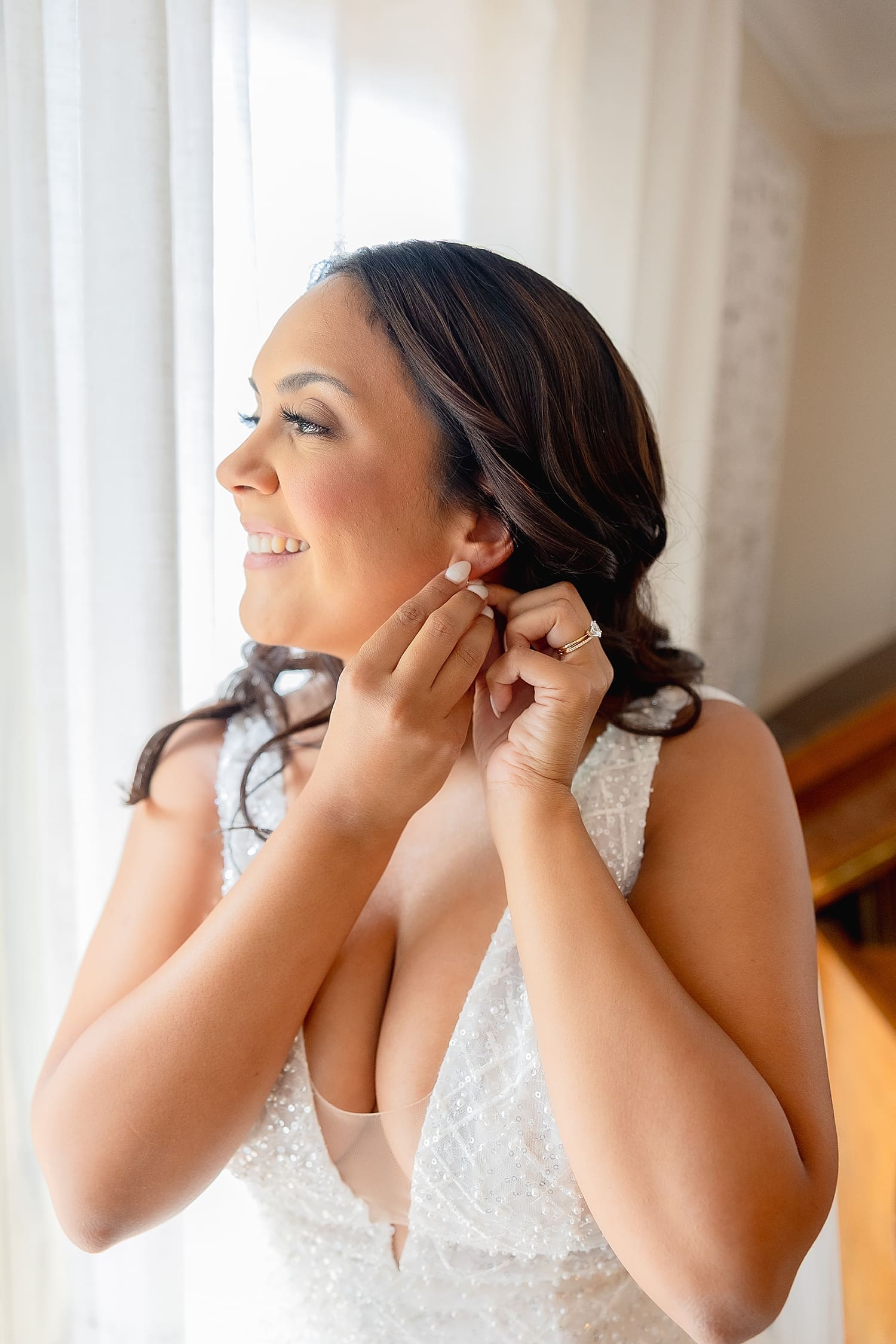 bride adjusts her earring next to a window by Southern California wedding photographer