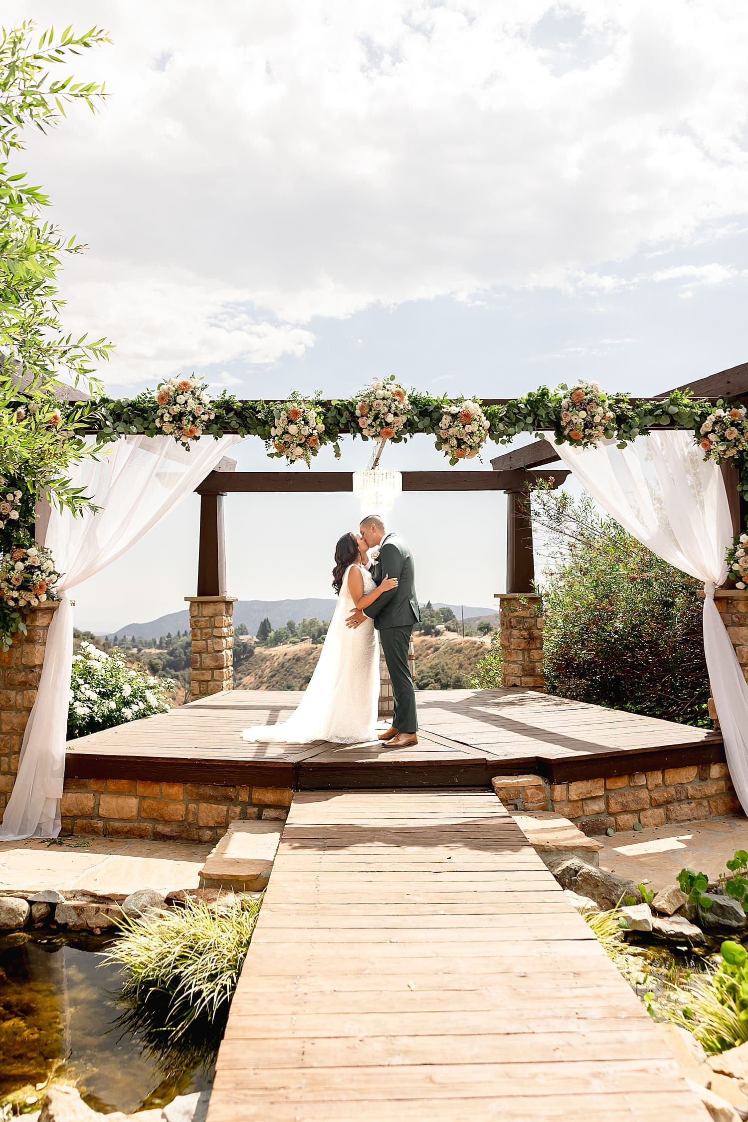 man and woman share a first kiss under large floral alter by Desiree Ashley Photography