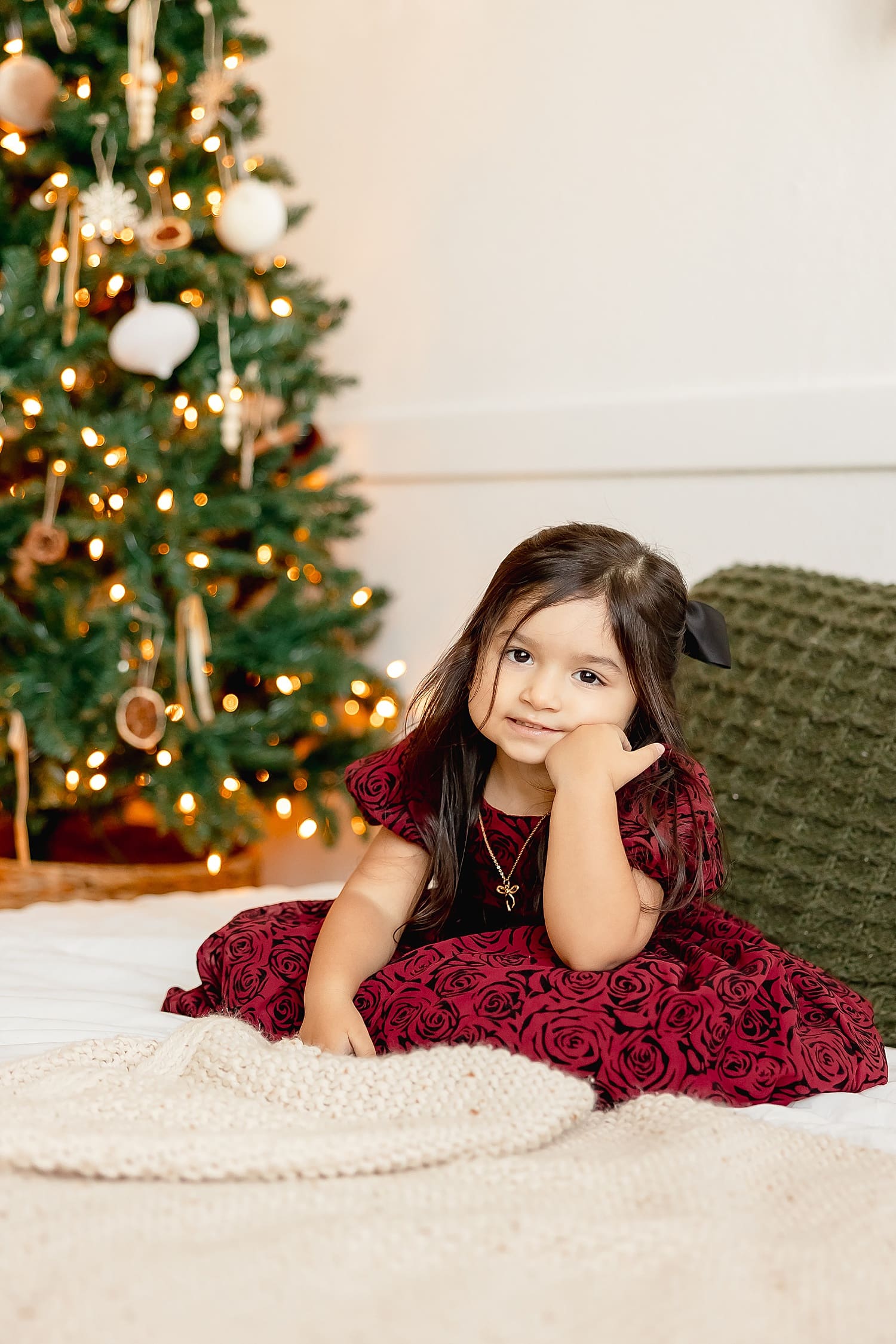 little girl sits on bed in front of christmas tree for holiday sessions