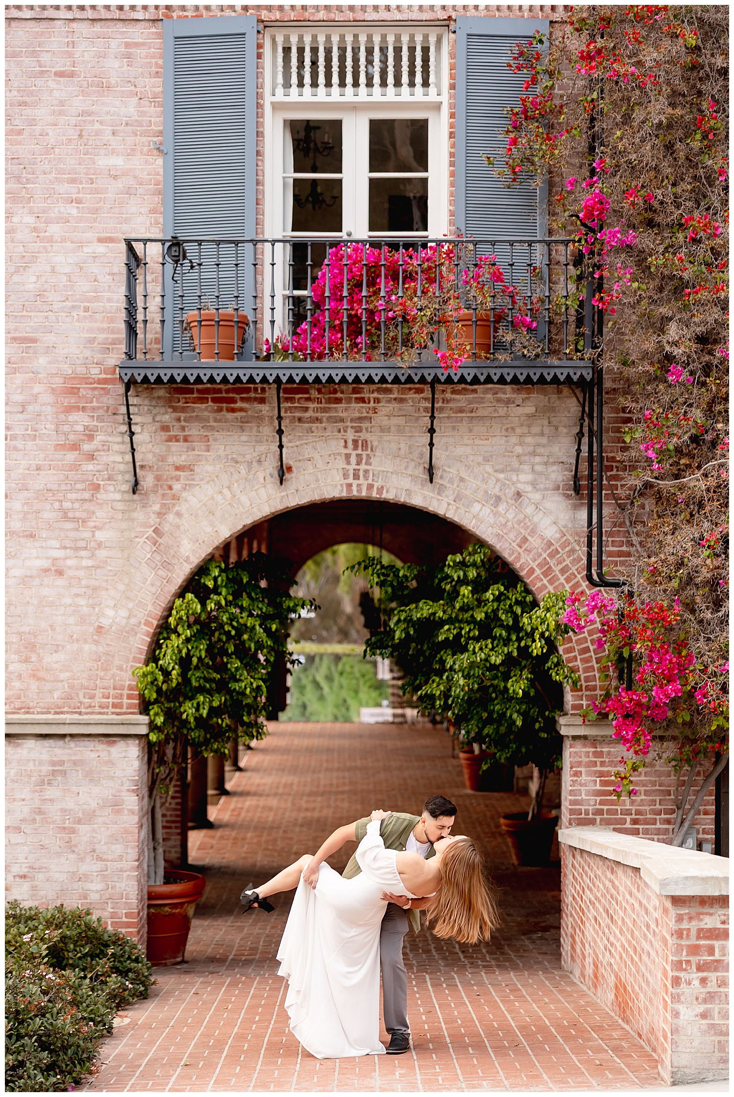man dips his fiance for a kiss under pink flowers by Southern California wedding photographer