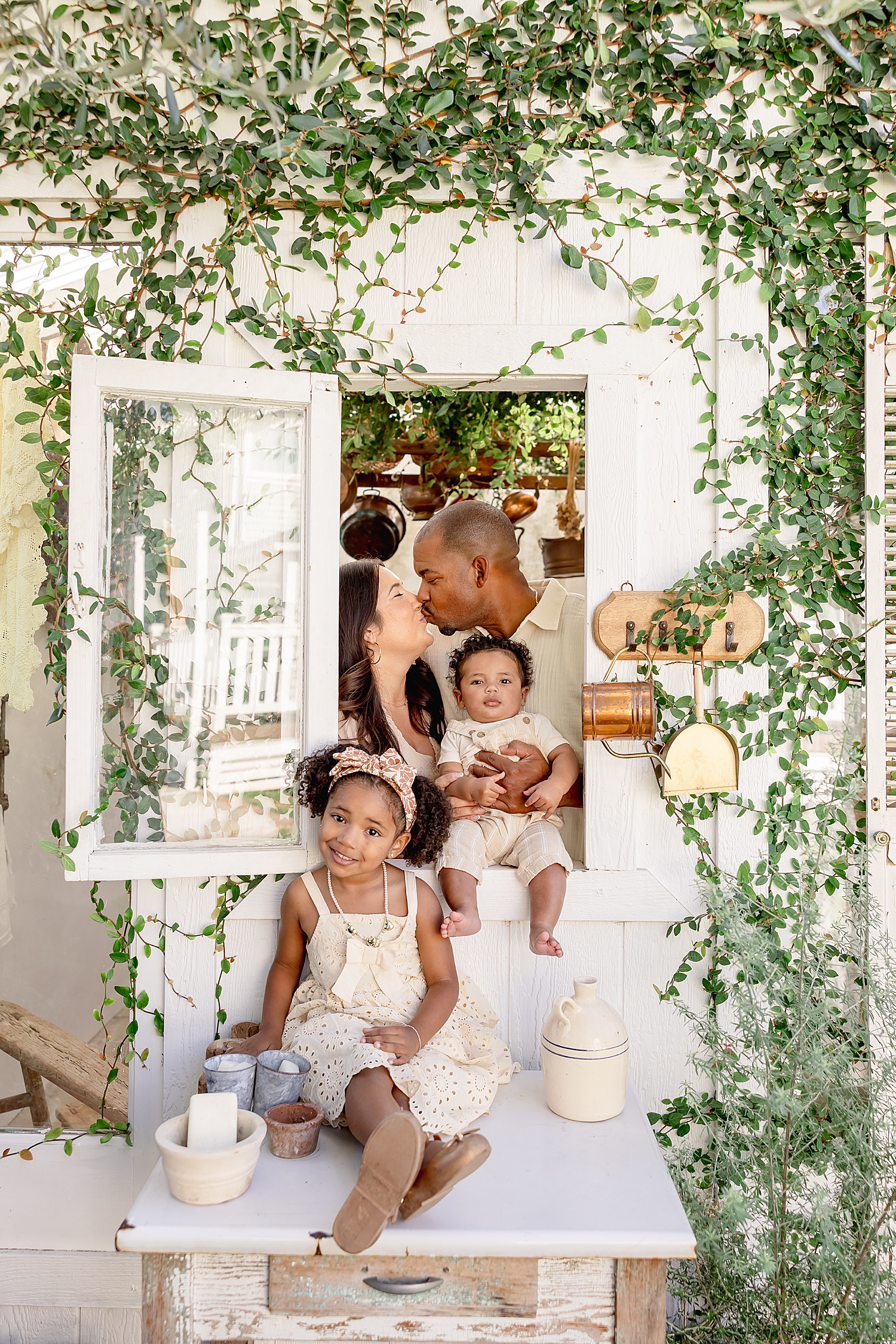parents share a kiss behind window while their kids smile for mini sessions