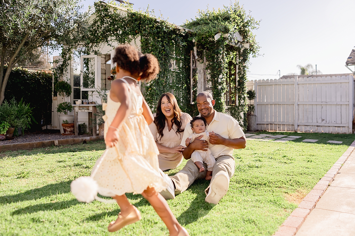 parents sit on grass while toddler runs around for mini sessions