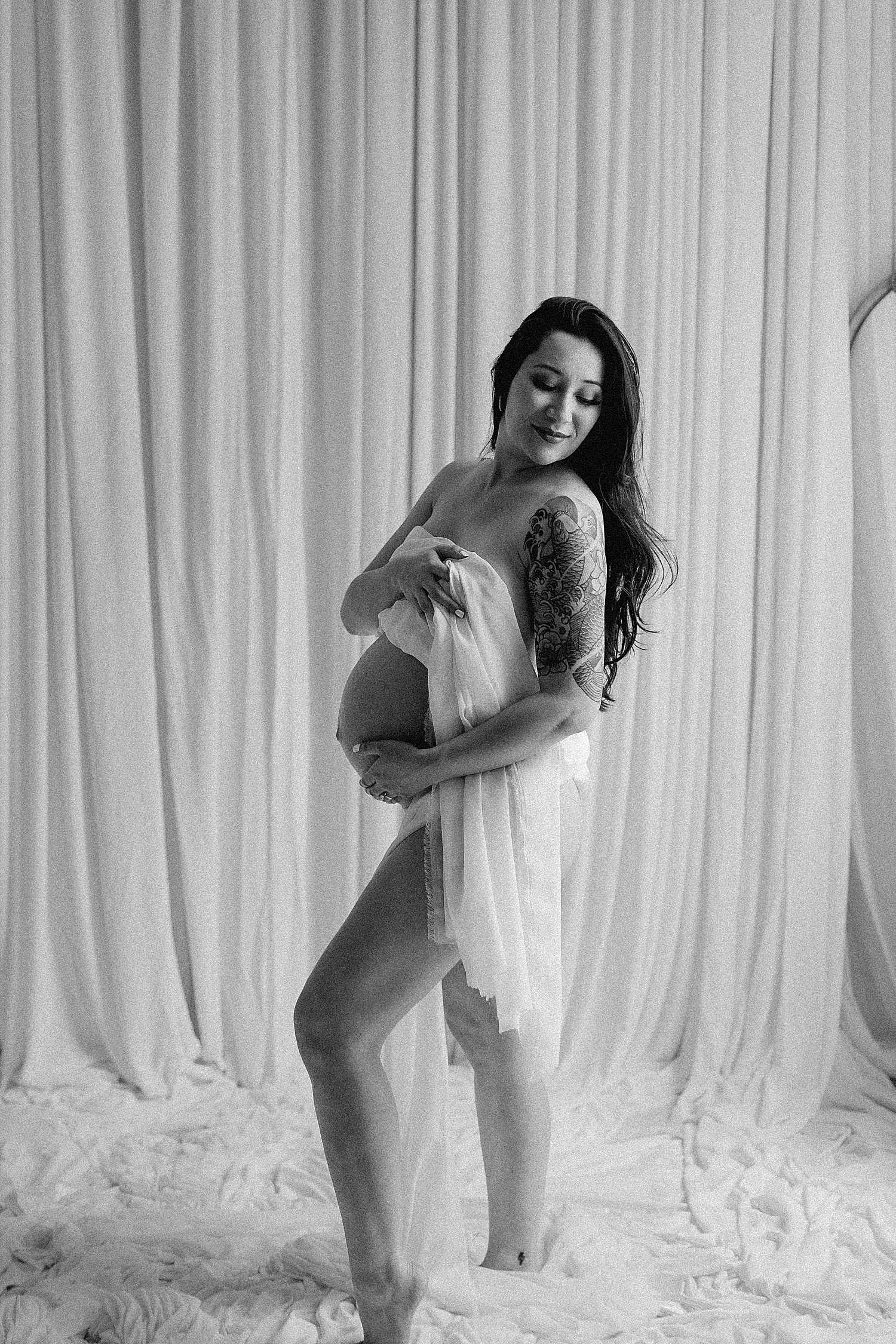 expecting mom stands in front of white drapes by Desiree Ashley Photography